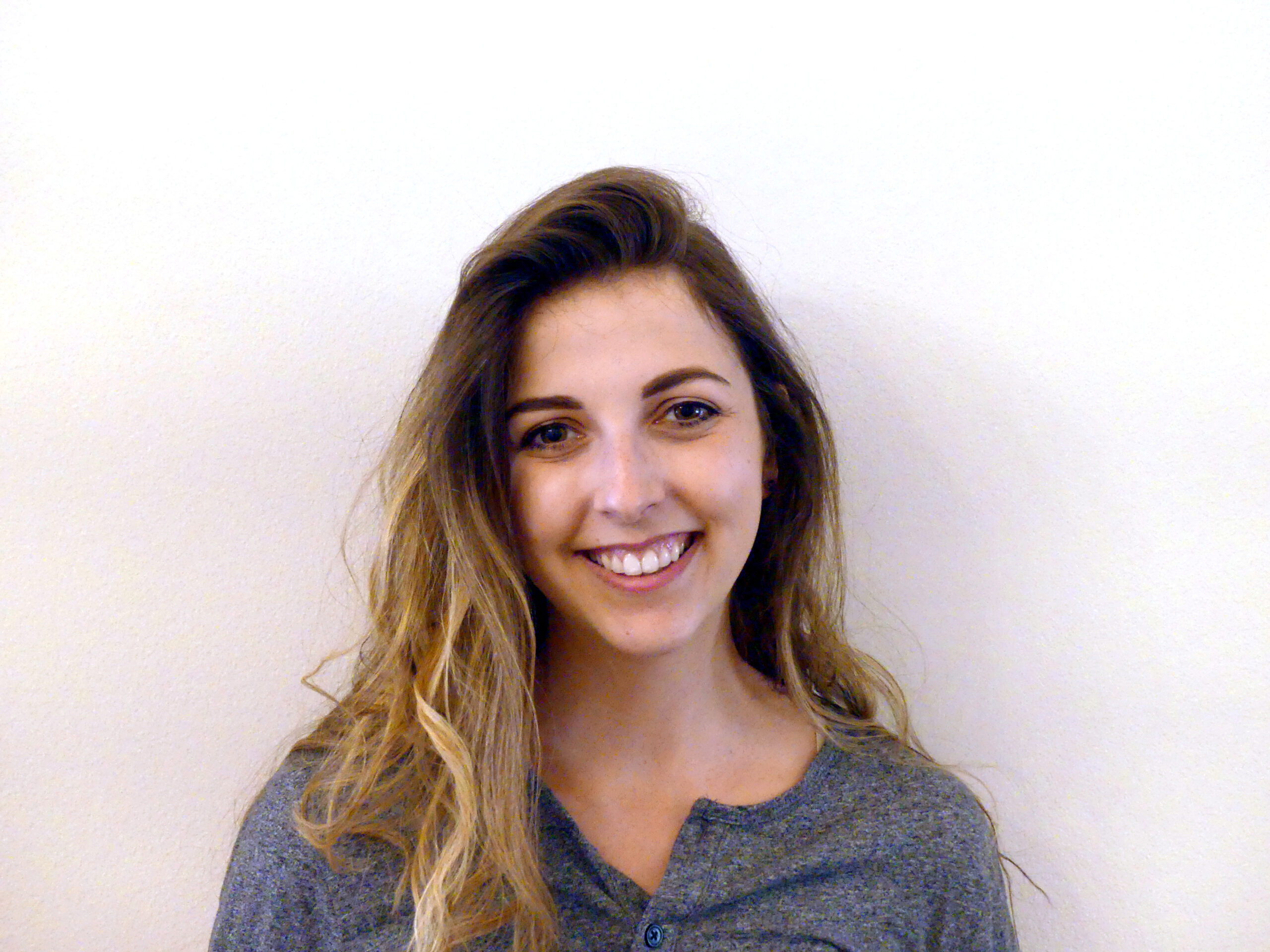 Jaime Grimm in a dark blue-gray top, in front of a white-cream background.