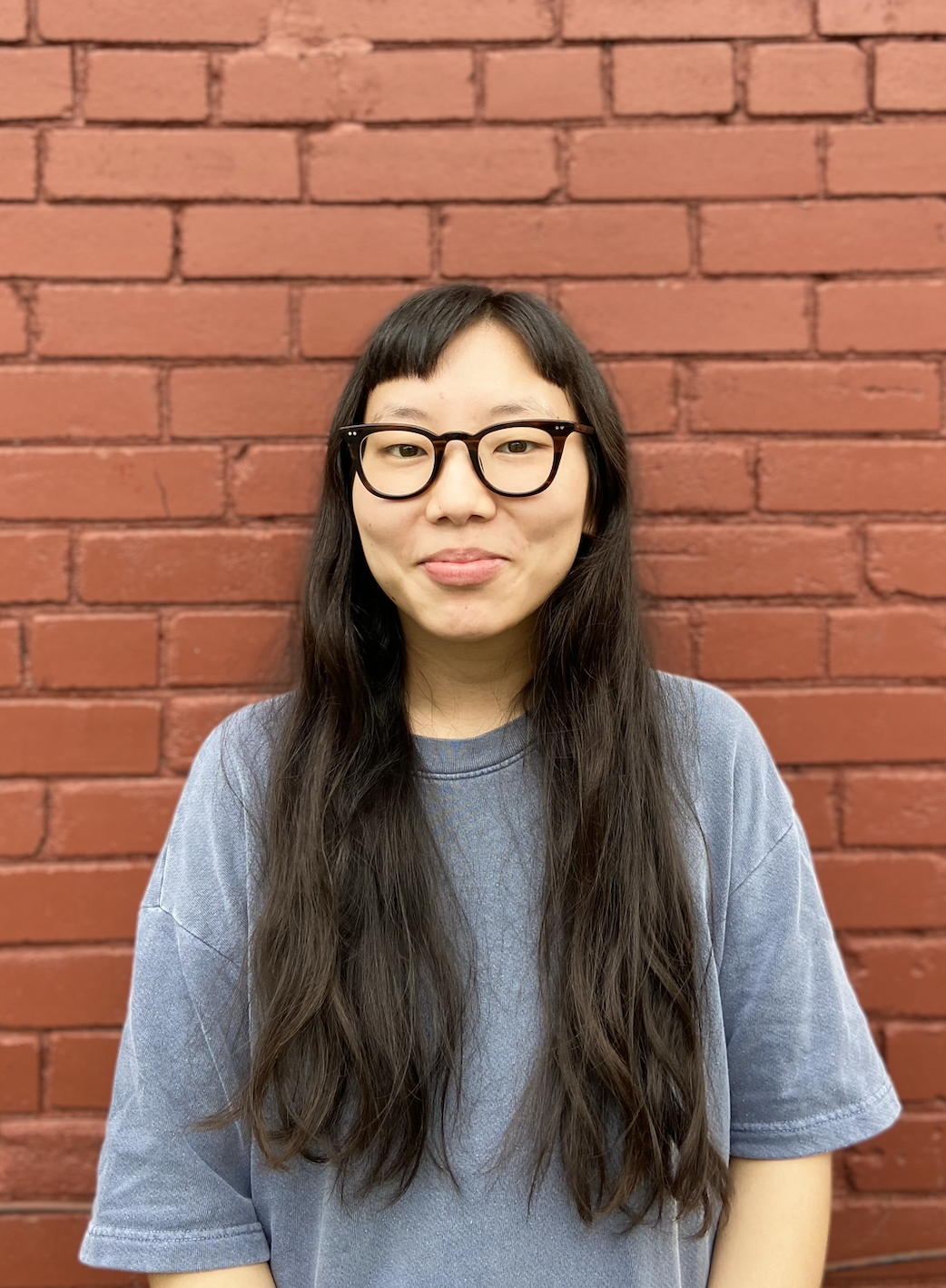 Tenzin Butsang in a blue t-shirt in front of a red brick wall.